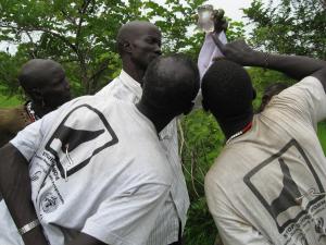 A field officer and village volunteers in South Sudan look at a sample of water containing copepods.